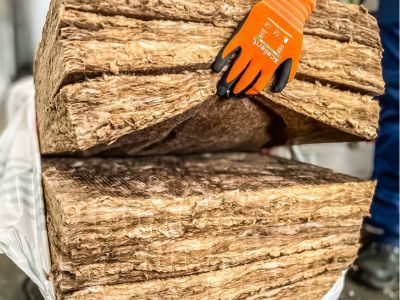 Hand mit Handschuh hält dicke Dämmstofflagen, zeigt Struktur und Dicke von Isoliermaterialien.